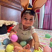 Julian joined the competition — help win amazing prizes! baby, bunny_ears, easter_eggs, bed, blanket, child, cute, smiling, indoors, toy, pastel_colors, holiday, playful, happy, person, young_child, decor, foot, hand, headwear