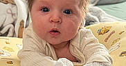 Aubrey is registered to the contest to win money with this photo: baby, infant, child, portrait, wide_eyed, surprised, bedhead, face, eyes, indoors, cushion, blanket, pajamas, mittens, seated, close_up, bedroom, soft_lighting, cartoon_pattern, adorable