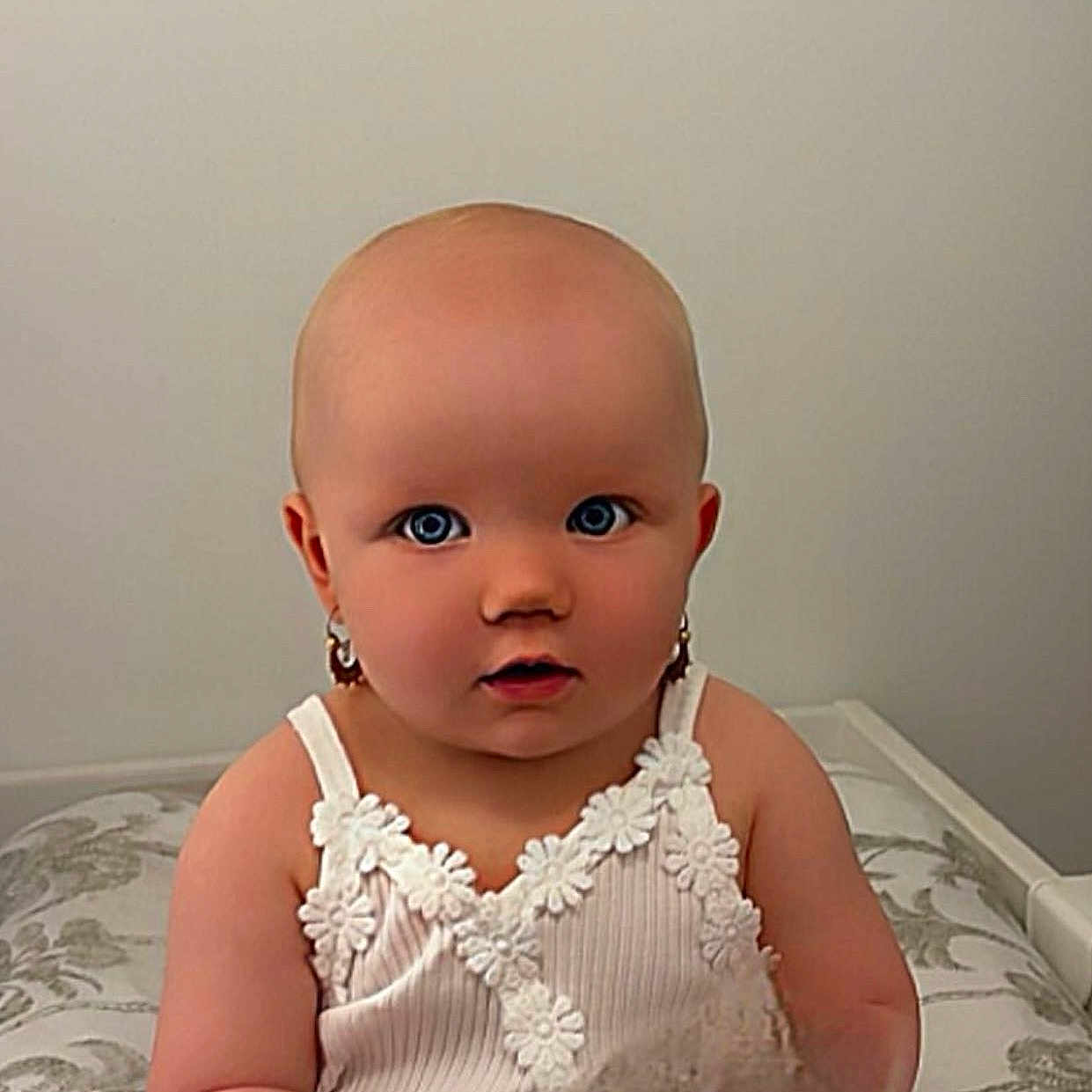 Mayana participe au concours pour gagner de l'argent avec cette photo : baby, child, curious, cushion, earrings, face, floral, head, indoor, infant, looking, patterned, person, portrait, shoulders, sitting, skin, white_top, wide_eyes, young