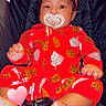 baby, infant, pacifier, red_onesie, headband, car_seat, black_background, sitting, cute, milk_carton_pattern, cookie_pattern, foot, hand, closeup, indoors, child, adorable, portrait, comfort, pink_heart
