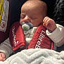 baby, sleeping, pacifier, car_seat, red, blanket, infant, child, clothing, face, hand, cozy, comfort, rest, young, cute, indoors, seatbelt, soft, peaceful