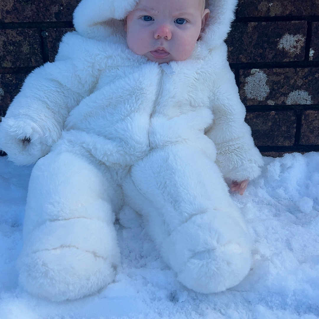 Elsie is registered to the contest to win money with this photo: baby, blue_eyes, brick_wall, child, cold, cute, face, fluffy, frozen, fur, headwear, outdoor, portrait, season, sitting, snow, snowsuit, warm, white, winter_clothing