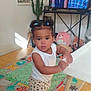 Kennedie participe au concours pour gagner de l'argent avec cette photo : toddler, child, indoor, playmat, table, television, cactus, stuffed_animal, toy, floor, pigtails, bracelet, pants, white_shirt, smiling_people_on_tv, decor, wooden_floor, living_room, plant, furniture
