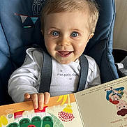 Oscar a rejoint le concours — aidez-le/la à gagner de superbes lots ! toddler, child, smiling, blue_high_chair, book, reading, illustration, turtle, rainbow, indoors, happy, cute, face, eyes, clothing, seatbelt, furniture, storytime, playful, colorful