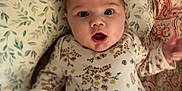 Ava is registered to the contest to win money with this photo: baby, infant, face, expression, clothing, floral_pattern, cushion, blanket, pink_pants, lying_down, indoors, child, cute, portrait, person, young, wide_eyes, open_mouth, soft_fabric, home