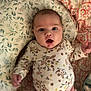 baby, infant, face, expression, clothing, floral_pattern, cushion, blanket, pink_pants, lying_down, indoors, child, cute, portrait, person, young, wide_eyes, open_mouth, soft_fabric, home
