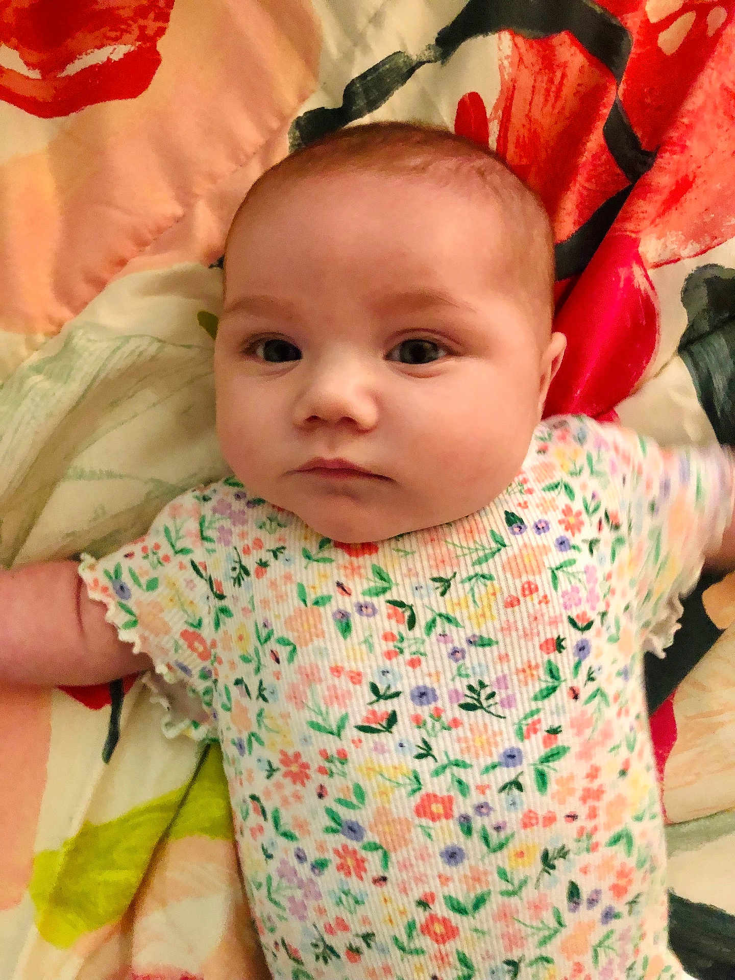Ava joined the competition — help win amazing prizes! baby, infant, floral_onesie, blanket, colorful, face, child, cute, lying_down, patterned_clothing, young_child, portrait, soft_lighting, indoors, skin, head, eyes, expression, small_person, peaceful