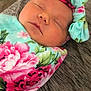 baby, sleeping, infant, headband, floral_pattern, blanket, closeup, peaceful, cozy, wrapped, portrait, child, soft, cute, indoors, resting, newborn, face, apparel, texture