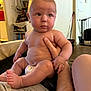 Grayson is registered to the contest to win money with this photo: adult_hand, arm, baby, blurred_background, book, bookshelf, child, diaper, face, foot, furniture, hand, home, indoor, living_room, person, shelf, sitting, skin, tattoo