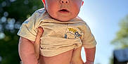 Grayson is registered to the contest to win money with this photo: arms, baby, child, clothing, cute, daytime, greenery, happy, holding, infant, nature, outdoor, person, portrait, shorts, sky, sunlight, tattoo, trees, tshirt
