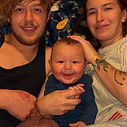 Grayson is registered to the contest to win money with this photo: baby, adult, family, smiling, indoor, blanket, tattoo, casual_clothing, couch, portrait, happy, hand_holding, person, young_adult, infant, home, relaxed, toddler, face, tshirt