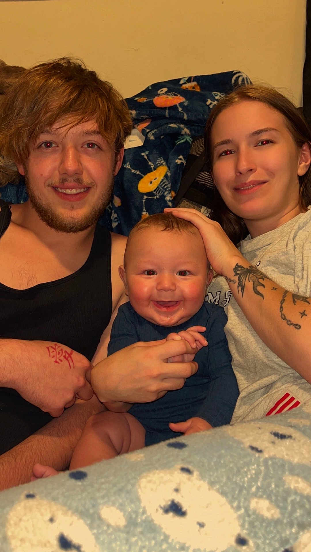 Grayson is registered to the contest to win money with this photo: baby, adult, family, smiling, indoor, blanket, tattoo, casual_clothing, couch, portrait, happy, hand_holding, person, young_adult, infant, home, relaxed, toddler, face, tshirt