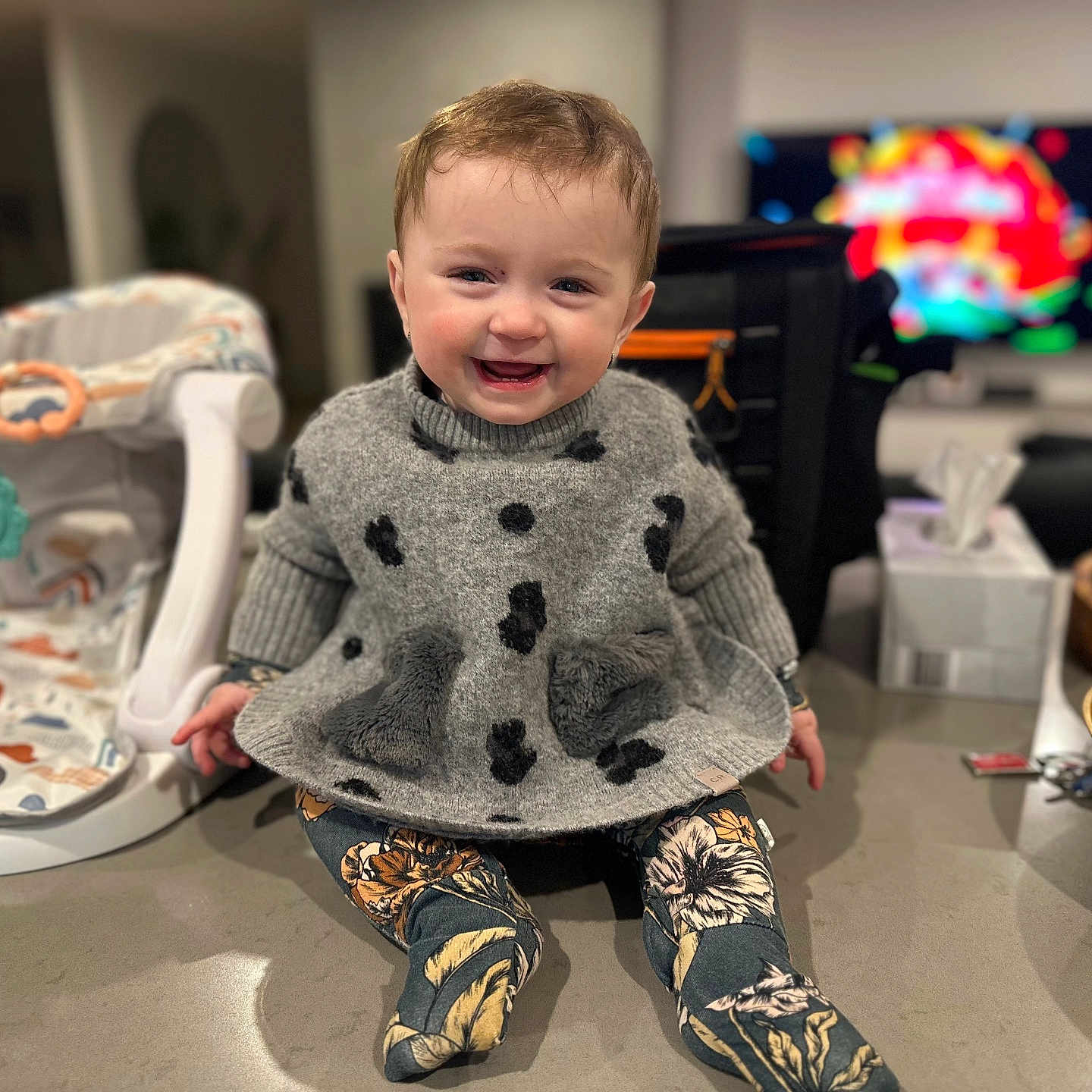 Dallas-Lee joined the competition — help win amazing prizes! apple, baby, baby_seat, blurred_background, clothing, face, fruit_bowl, happy, head, indoor, infant, kitchen_counter, leggings, pear, person, sitting, smiling, sweater, television, tissue_box