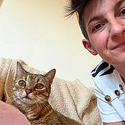 Newt participe au concours pour gagner de l'argent avec cette photo : cat, tabby_cat, person, portrait, smiling, couch, blanket, pillow, indoor, home, pet, companion, whiskers, brown_fur, blue_eyes, short_hair, casual_clothing, tattoo, selfie, cozy