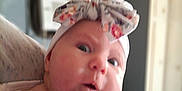 Evelyn is registered to the contest to win money with this photo: baby, infant, headband, floral, hand, skin, face, indoor, person, cute, expression, closeup, portrait, newborn, child, apparel, holding, curious, soft_light, human
