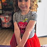 Luna joined the competition — help win amazing prizes! blue_eyes, bow, child, curly_hair, cute, decor, fashion, floor, girl, happy, home, indoor, person, portrait, pose, red_skirt, smiling, striped_shirt, toy, young