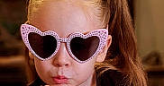 Luna is registered to the contest to win money with this photo: accessory, black_shirt, blowing_kiss, child, closeup, cute, expression, face, fashion, flower, girl, hair, headband, heart_shaped, indoor, pigtails, pink, playful, portrait, sunglasses
