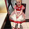 child, girl, dress, red_bow, red_shoes, white_tights, chair, indoor, mall, floor_tiles, black_chair, people, walking, reflection, pale_skin, short_hair, looking_down, seated, cute, fashion