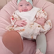 Maddison joined the competition — help win amazing prizes! baby, child, infant, smiling, headband, bow, dress, floral, footwear, cushion, pink, soft, happy, cute, indoors, person, young_child, seated, playful, comfort