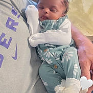 Makenzie is registered to the contest to win money with this photo: baby, sleeping, infant, onesie, floral_pattern, mittens, socks, lace, adult_hand, grey_shirt, purple_text, closeup, indoor, resting, peaceful, portrait, toddler, cute, child, holding