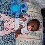 baby, pacifier, plush_toy, stitch, blanket, pajamas, bib, patterned_sheet, laundry_basket, infant, sleepwear, toy, pink, blue, floral, cute, child, lying_down, indoors, comfort