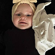 Charlie a rejoint le concours — aidez-le/la à gagner de superbes lots ! baby, headband, blanket, face, infant, clothing, smile, portrait, cute, black_top, brown_pants, soft_toy, star_pattern, lying_down, indoors, child, young, baby_girl, fabric, cozy