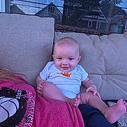 Luca is registered to the contest to win money with this photo: baby, smile, infant, onesie, person, couch, window, reflection, house, tree, outdoor, shirt, red_shirt, skin, foot, hand, relaxing, seated, home, casual