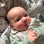 Arthur is registered to the contest to win money with this photo: baby, infant, face, tongue, hand, clothing, blanket, soft_toy, cute, rosy_cheeks, closeup, cozy, sleepwear, person, portrait, indoors, expression, child, newborn, skin