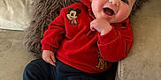 Arthur is registered to the contest to win money with this photo: baby, smiling, red_sweater, mickey_mouse, navy_pants, striped_socks, couch, pillow, indoor, child, happy, cute, portrait, comfort, infant, sitting, cozy, clothing, face, hand