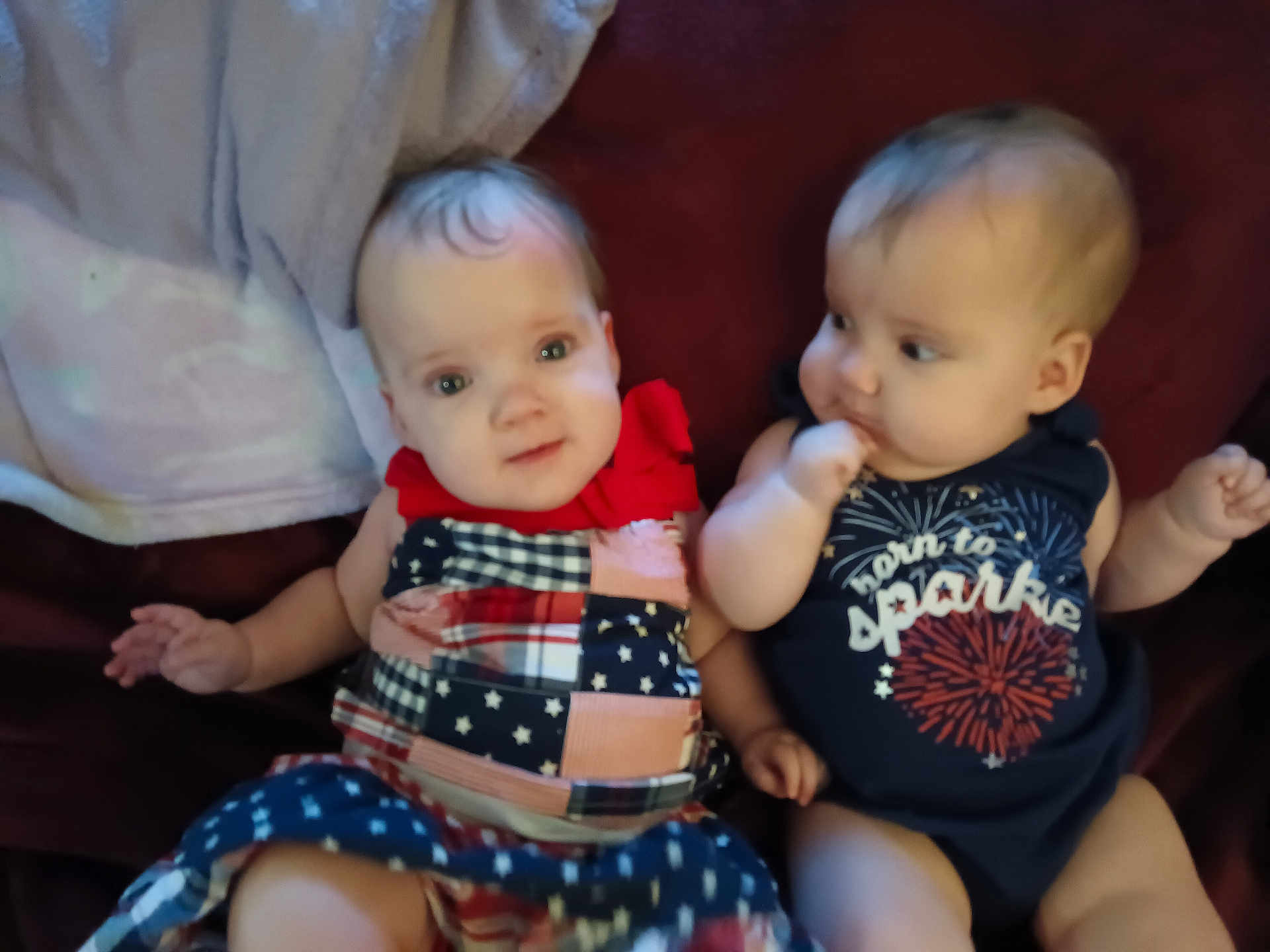 Zayleigh joined the competition — help win amazing prizes! baby, infant, child, couch, clothing, dress, onesie, red_bow, fireworks, sitting, face, cute, indoor, portrait, two_children, expression, curious, skin, head, person