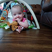Zayleigh joined the competition — help win amazing prizes! baby, child, toy, plush_toy, play_mat, floor, living_room, couch, adult, person, furniture, wood_floor, play_gym, smiling, indoor, family, happy, curly_hair, casual_clothing, people