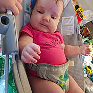 Zaylynn is registered to the contest to win money with this photo: baby, infant, child, pink_shirt, baby_seat, toy, hand, face, clothing, indoor, seatbelt, furniture, expression, person, toddler, room, household_items, colorful, candid, casual