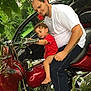 Rebel joined the competition — help win amazing prizes! toddler, child, man, motorcycle, red_motorcycle, outdoor, greenery, parked_car, white_shirt, jeans, curly_hair, barefoot, tattoo, handlebars, chrome, vehicle, father_and_son, daytime, person, nature