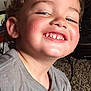 child, smiling, face, curly_hair, teeth, gray_shirt, indoor, carpet, happy, close_up, person, cute, playful, young, toddler, casual, portrait, candid, cheeky, light