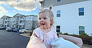 Ellia is registered to the contest to win money with this photo: adult, apartment_building, arm, beanie, blue_sky, car, child, cloud, hair_bun, happy, holding, outdoors, parking_lot, person, portrait, sky, smile, street, tattoo, toddler