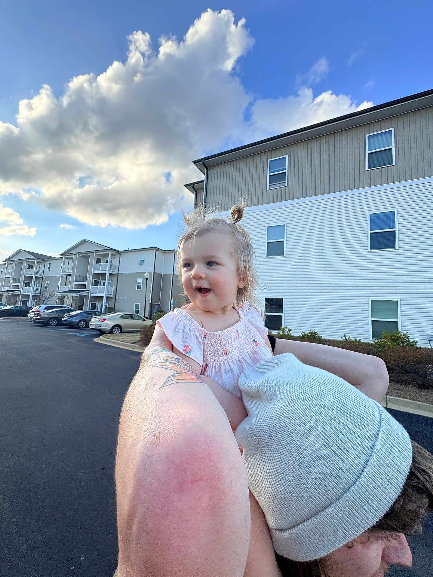 Ellia is registered to the contest to win money with this photo: toddler, child, person, adult, beanie, hair_bun, smile, outdoors, apartment_building, parking_lot, car, tattoo, arm, sky, cloud, blue_sky, holding, happy, portrait, street