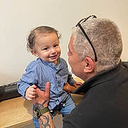 Kays participe au concours pour gagner de l'argent avec cette photo : adult, arm, child, face, glasses, hair, hand, happy, holding, indoor, interaction, jeans, person, shirt, smile, table, tattoo, toddler, watch, wood