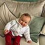 baby, child, infant, knitted_sweater, red_tights, bows, couch, pillows, smile, face, hand, hair_clip, indoors, cozy, cute, sitting, soft_furniture, portrait, happy, warm_clothing