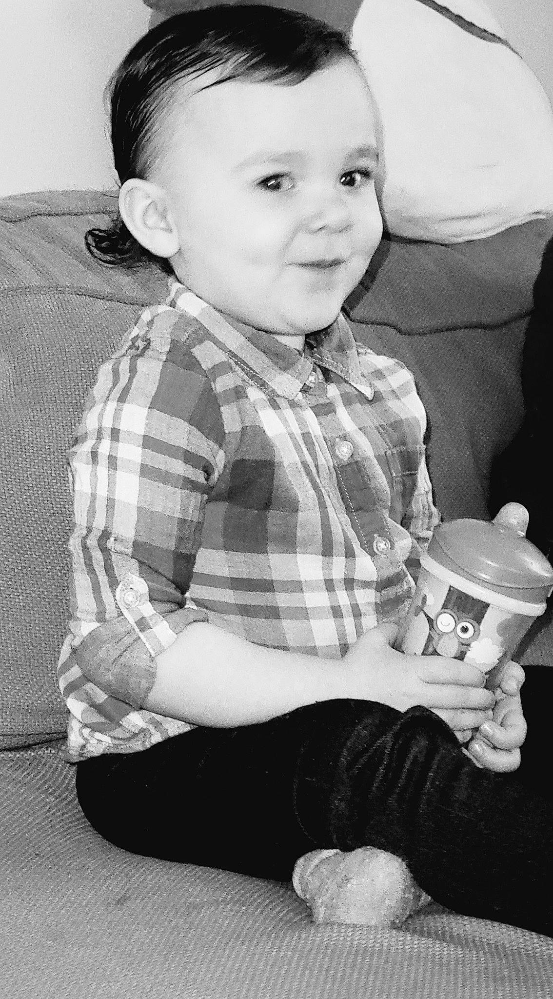 Kali is registered to the contest to win money with this photo: arm, baby_toddler_clothing, black, black_and_white, dress_shirt, drinkware, face, flash_photography, gesture, hand, head, organ, person, photograph, product, sleeve, smile, standing, style, tartan