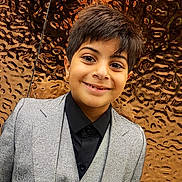 Adam joined the competition — help win amazing prizes! black_clothing, boy, bronze, child, dress_shirt, facial_expression, fashion, formalwear, gray_clothing, indoor, looking_at_camera, metallic_background, photography, portrait, short_hair, smiling, standing, suit, textured_wall, vest
