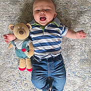 Hudson joined the competition — help win amazing prizes! baby, teddy_bear, striped_shirt, jeans, rug, child, smiling, cute, toy, indoor, patterned_rug, happy, infant, clothing, playful, lying_down, soft_toy, person, casual_wear, joyful