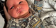 Liam joined the competition — help win amazing prizes! newborn, baby, infant, clothing, onesie, pattern, hand, quilt, blanket, bed, face, person, sleepwear, skin, cute, young, portrait, indoor, resting, comfort