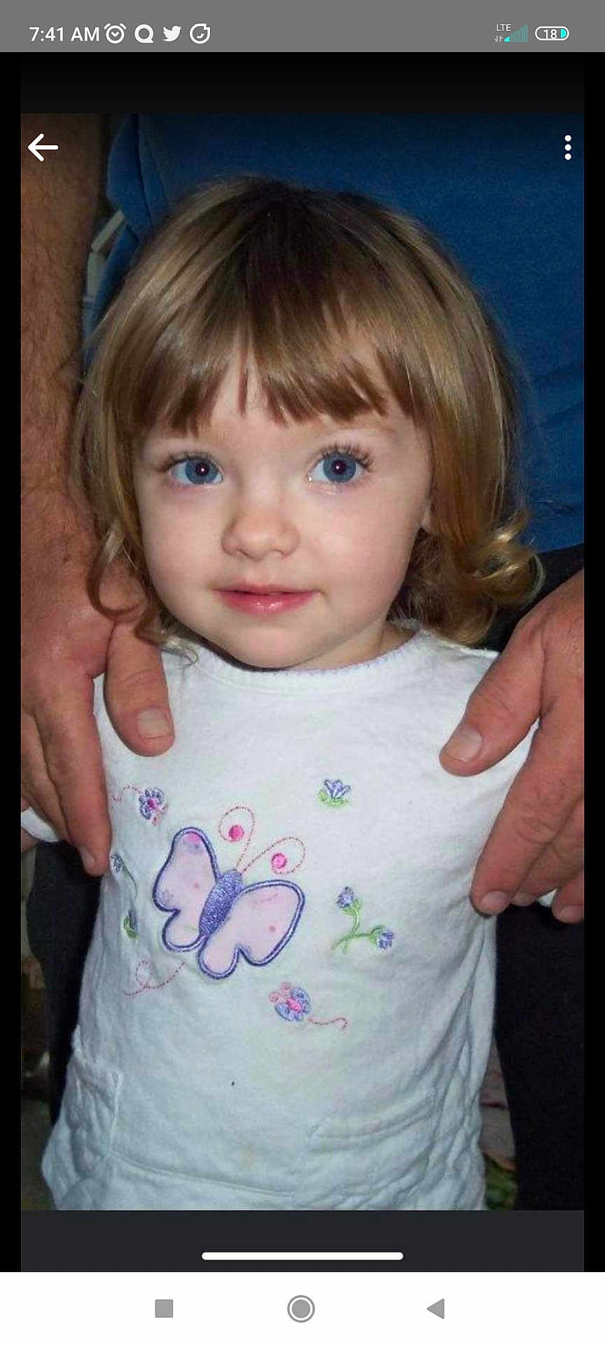 Vera is registered to the contest to win money with this photo: child, toddler, blue_eyes, curly_hair, white_shirt, butterfly_design, hands, adult_hands, portrait, indoor, person, cute, young_child, standing, looking_up, casual_clothing, close_up, human, smiling, childhood