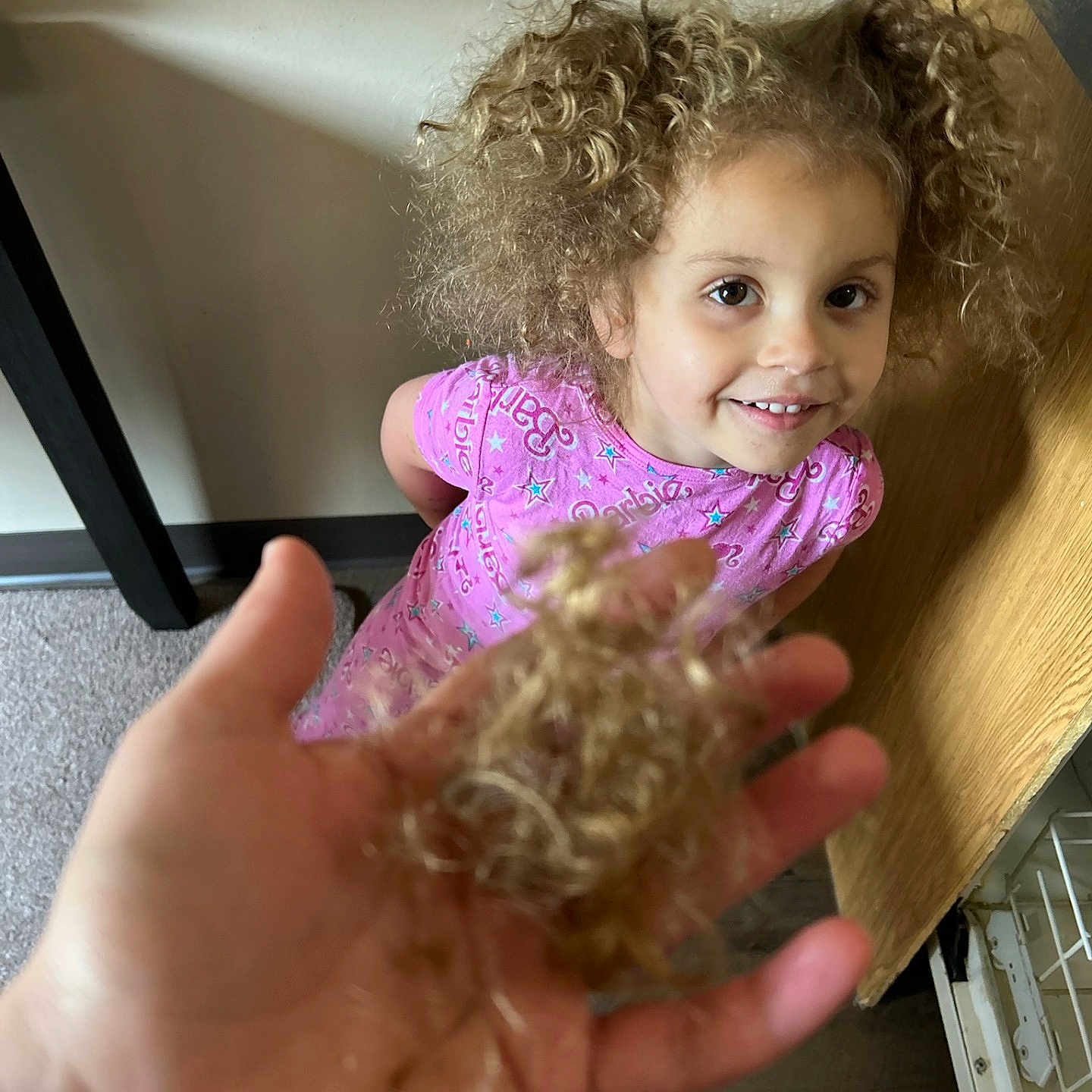 Austyn is registered to the contest to win money with this photo: background_wall, bright, cabinet, carpet, child, closeup, curly, curly_hair, expression, face, hair, haircut, hand, indoor, person, pink_clothing, playful, smile, wood_floor, young
