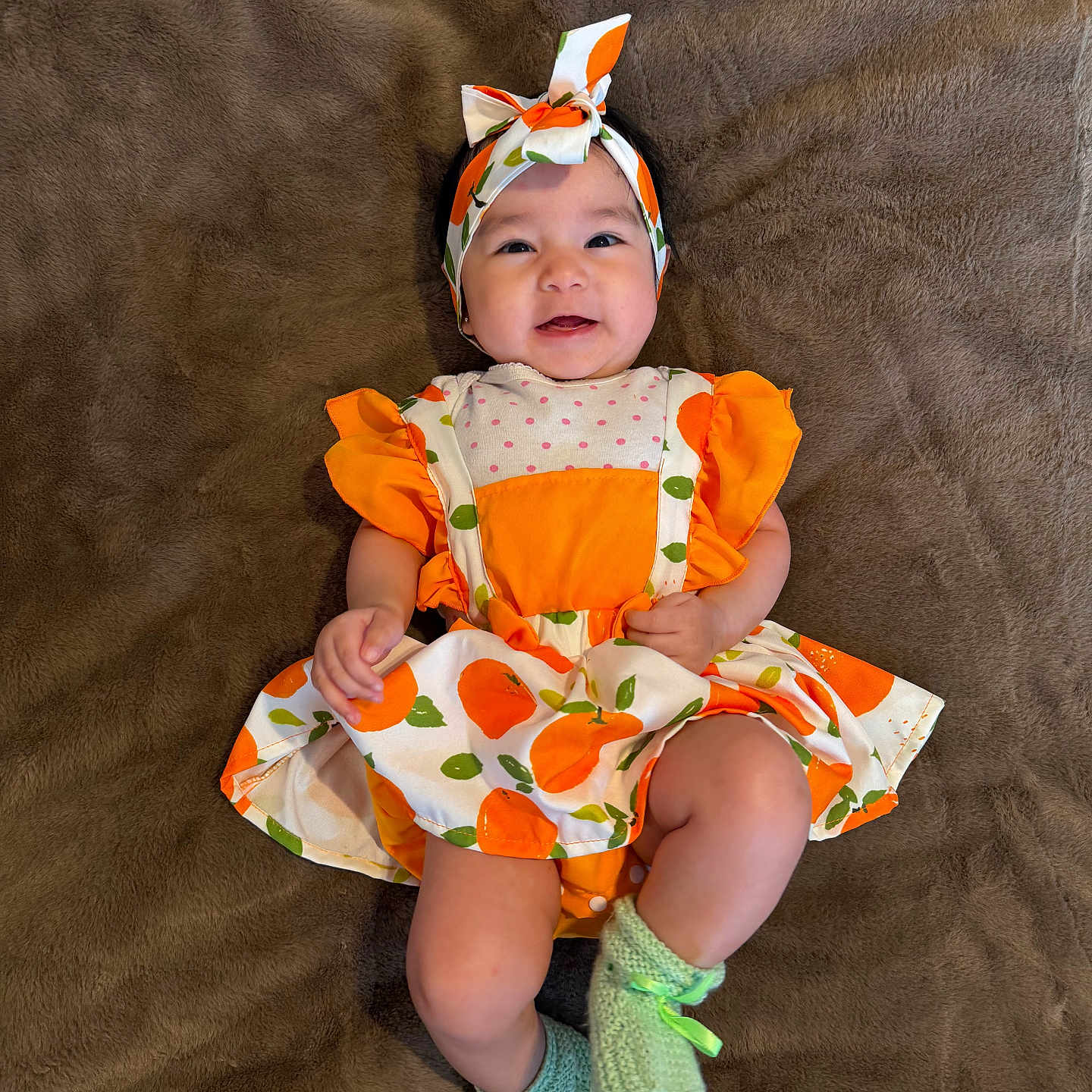 Brielle Amarra is registered to the contest to win money with this photo: baby, blanket, booties, bow, child, cute, hands, happy, headband, indoor, infant, knitted_booties, legs, lying_down, orange_dress, patterned_dress, plush_blanket, polka_dot, portrait, smiling