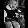 Mélody participe au concours pour gagner de l'argent avec cette photo : black_and_white, casual_clothing, child, container, face, hair, happy, holding, hoodie, indoor, jacket, pants, patterned_seat, playful, portrait, seat, sitting, smiling, toy, young_child