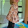 blouse, cabinet, child, cute, dinosaur, face, floor, furniture, hair, happy, hearts, indoor, leggings, person, play_mat, shoes, smiling, standing, toddler, toy