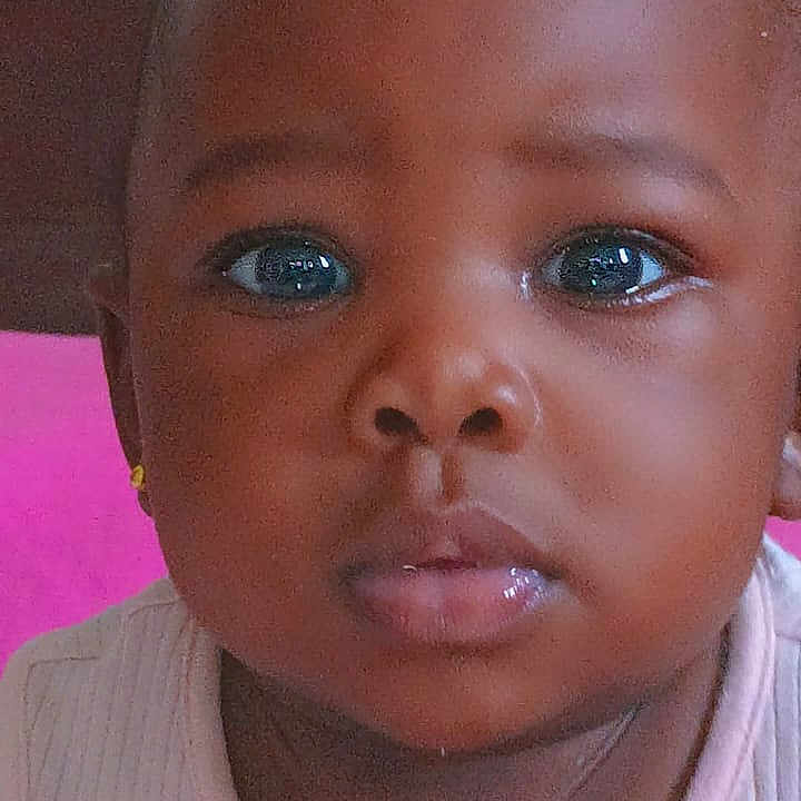 Marie a rejoint le concours — aidez-le/la à gagner de superbes lots ! adorable, baby, child, close_up, clothing, curly_hair, cute, ears, expression, eyebrows, face, indoors, infant, lips, looking_at_camera, person, pink_background, portrait, skin, young_child