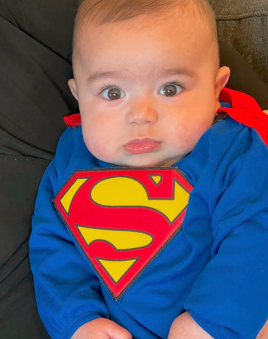 Kalel is registered to the contest to win money with this photo: arm, azure, baby, baby_toddler_clothing, cheek, chin, forehead, hair, human_body, iris, mouth, muscle, neck, nose, orange, person, skin, sleeve, standing, superman