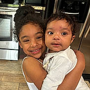 Layal joined the competition — help win amazing prizes! appliance, baby, child, curly_hair, cute, family, flooring, happy, home, hugging, indoor, kitchen, person, portrait, refrigerator, sibling, smiling, stove, white_clothing, young